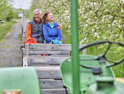 Paar sitzt in Hänger und lässt sich von Trecker durch die Plantage ziehen.