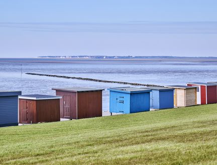 Bunte Badebuden stehen an der Promenade und dahinter ist das Wattenmeer zu sehen